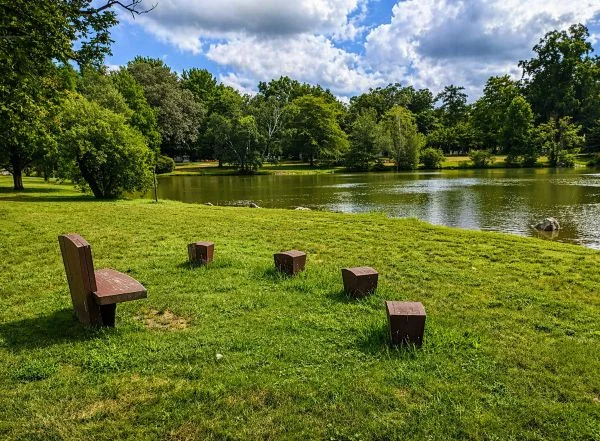 Peaceful lakeside view at Jamaica Plain, MA Cemeteries with wooden seats, green lawn, and trees