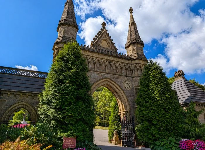 Gothic entrance arch at Boston, MA cemeteries with stone towers, iron gate, and landscaped grounds