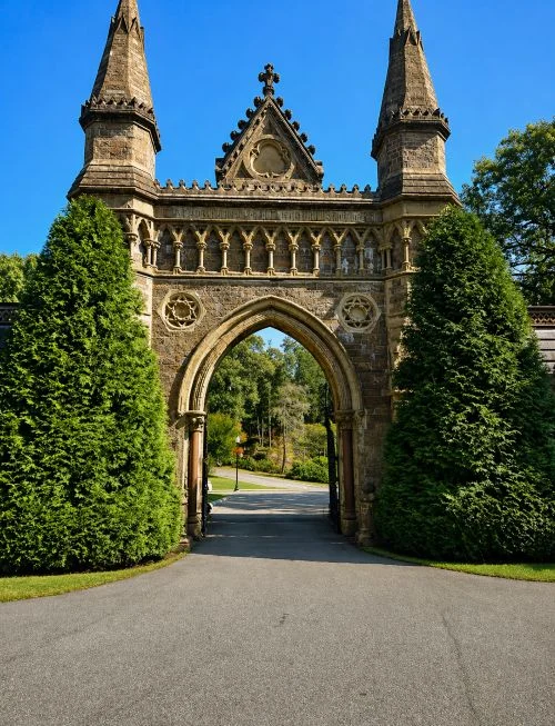 Historic stone gateway at Quincy, MA cemeteries with Gothic arch, twin spires, and evergreen trees