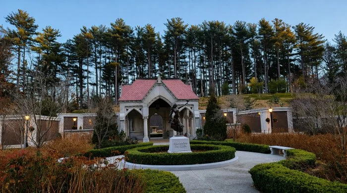 Landscaped memorial pavilion at Quincy, MA cemeteries with statue, garden paths, and mausoleum walls